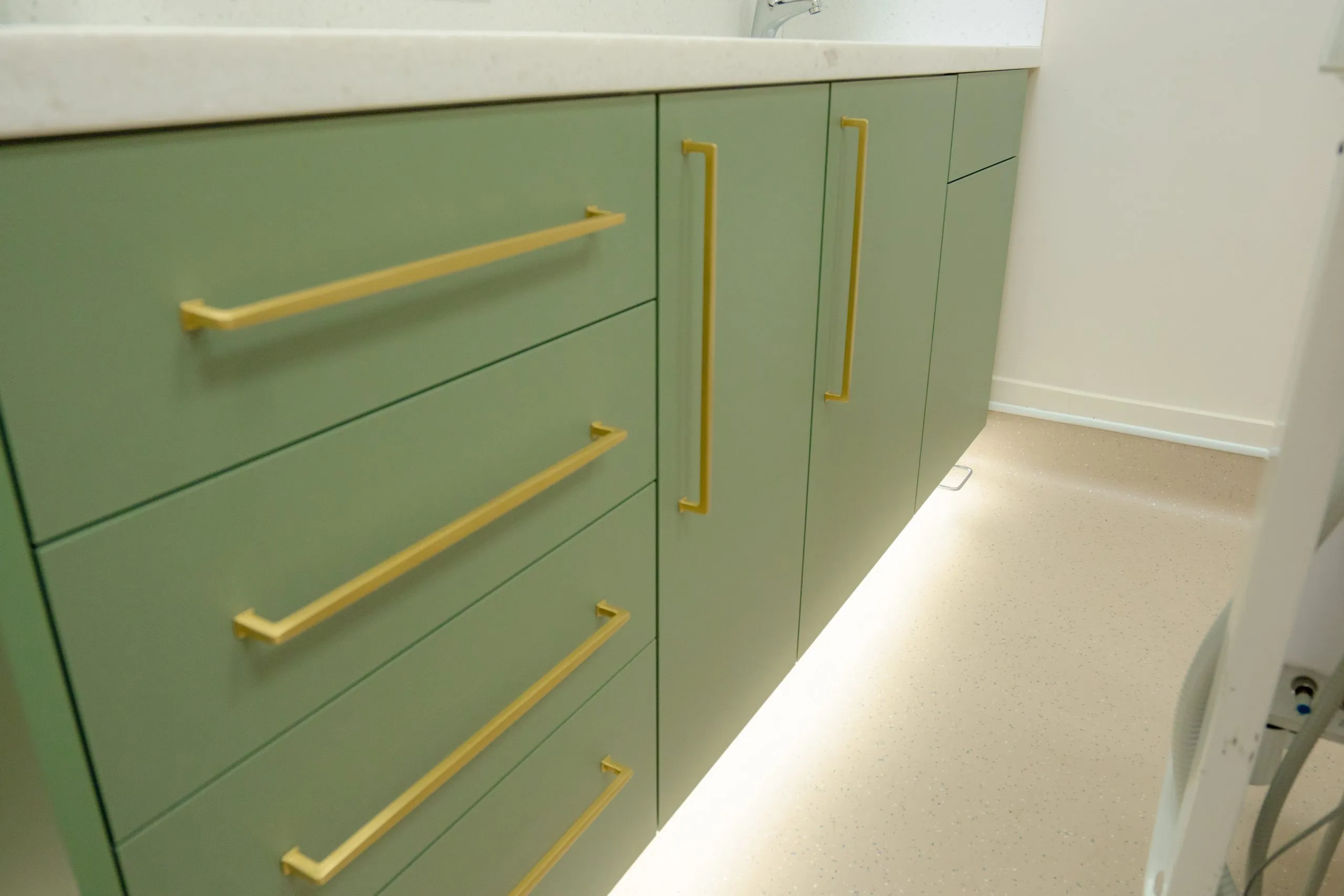 Bespoke sage-green dental cabinetry with antique brass handles at Alma Dental